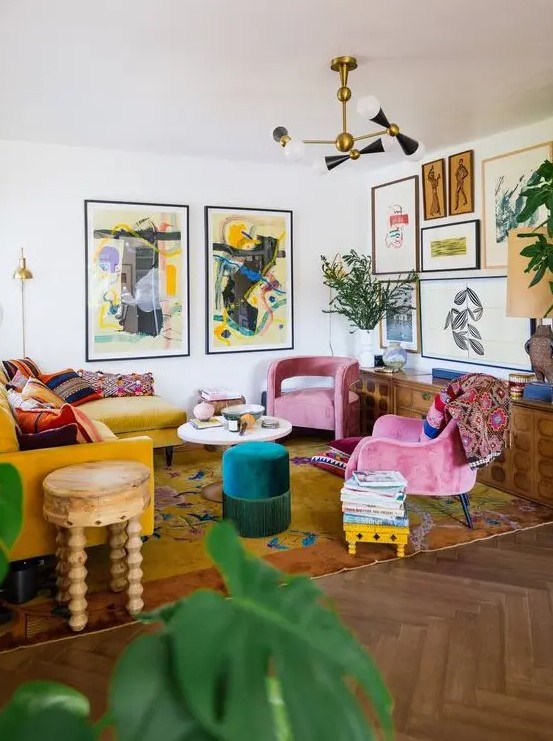 A bold maximalist living room with a mustard sectional, pink chairs, an emerald pouf, a bold gallery wall and a bright rug plus statement plants.