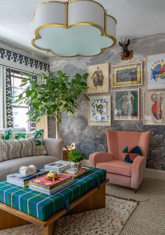 A bold maximalist living room with printed wallpaper, a grey sofa, a pink chair, an ottoman and a bright gallery wall.
