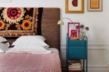 a bright eclectic bedroom with an upholstered bed, a wooden chest, a bight vintage nightstand and abstract art