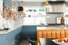 a bright eclectic kitchen with dusty blue cabinets, white marble countertops, a kitchen island, an amber leather sofa, pendant lamps