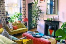 a bright maximalist living room with pink walls, mustard and neon green furniture, a vintage fireplace, a red ottoman and some statement plants