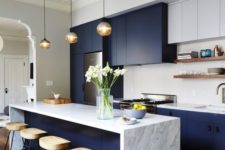 a bright navy and white galley kitchen with a stone countertop, pendant lamps, wooden stools and a white tile backsplash