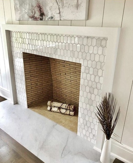 A built in non working fireplace clad with metal elongated hex tiles and with a white wooden frame
