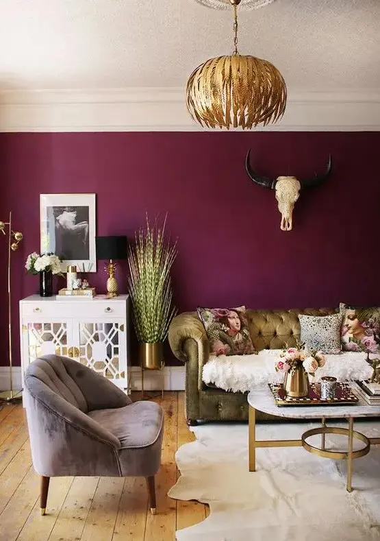 Featuring a captivating purple accent wall, this eclectic living room blends a luxurious gold sofa with a subtle grey chair. A bold gold chandelier hangs above a chic coffee table and a mirror cabinet, enhancing the room's dynamic.