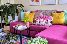 a cheerful living room with a hot pink sectional, colorful pillows and artworks, a bright rug, potted plants and a mirror to add space to it