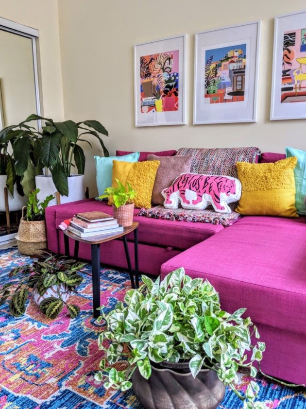 a cheerful living room with a hot pink sectional, colorful pillows and artworks, a bright rug, potted plants and a mirror to add space to it