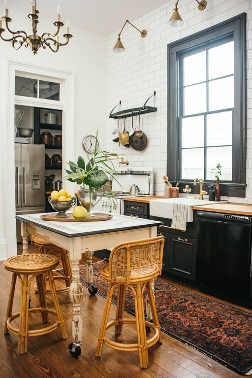 a chic kitchen pairing black cabinets with neutral countertops, a shabby chic table, vintage rattan chairs and industrial lamps