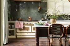 a chic moody eclectic kitchen with white cabinets, a vintage cooker, a copper hood, pendant lamps, a large kitchen island in vintage style