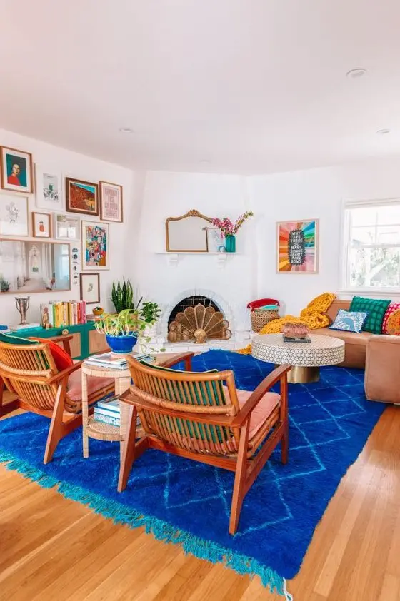 A colorful eclectic living room with a fireplace, a coffee table, a couple of pink chairs, a super bold rug and an emerald credenza.