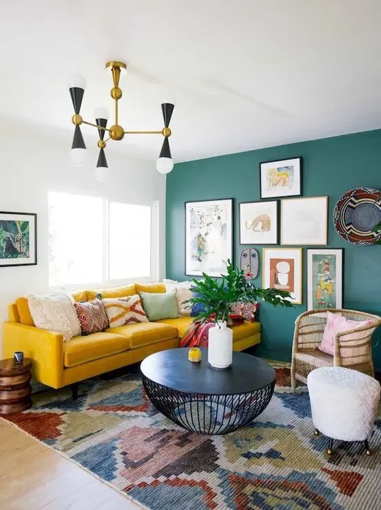 A colorful eclectic living room with a green statement wall with artworks, a boho rug, a mustard sofa and wicker touches.