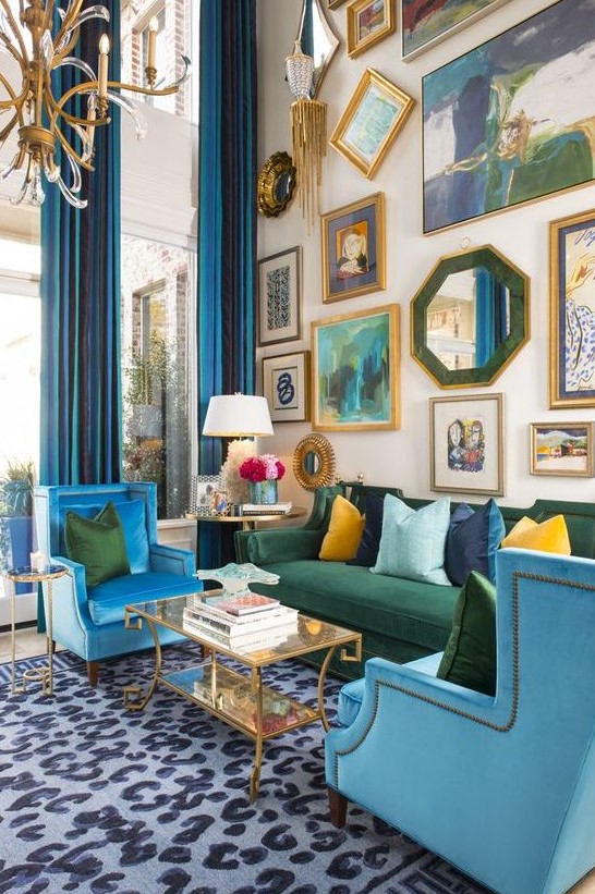 A colorful maximalist living room with double height ceilings, a neutral floor with a printed rug, blue and green furniture, a bold gallery wall.