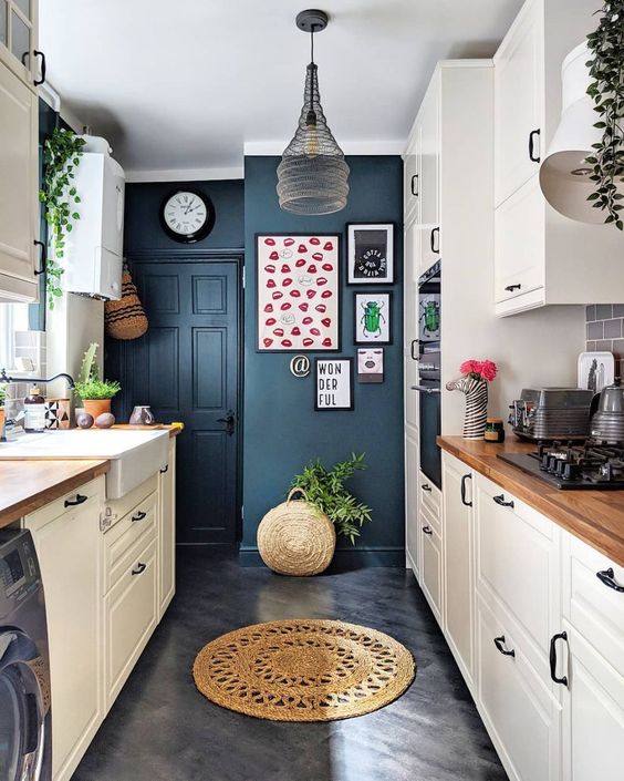 a contemporary kitchen with navy walls, white cabinets with wooden countertops and a catchy pendant lamp