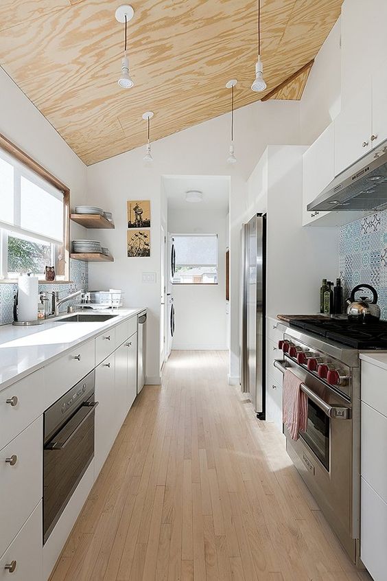 a contemporary white galley kitchen with a plywood ceiling with penddant lamps, a wooden floor and a blue tile backsplash
