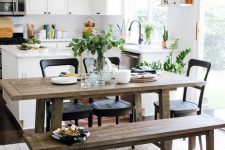 a cool eclectic kitchen with white cabinets, a white kitchen backsplash, a rustic dining set with benches, black chairs and a black pendant lamp