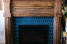 a fireplace with blue elongated hex tiles around and a rustic wooden mantel and frame for a farmhouse feel