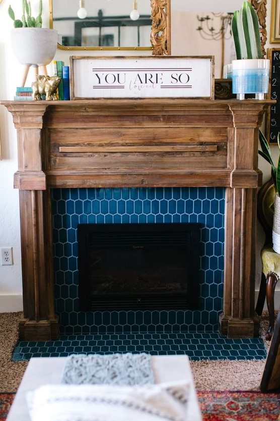a fireplace with blue elongated hex tiles around and a rustic wooden mantel and frame for a farmhouse feel
