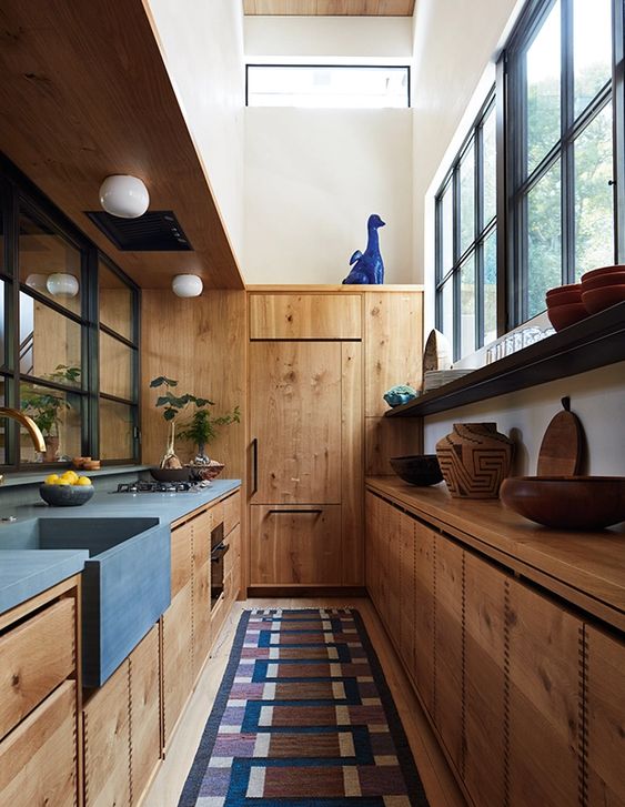 a galley kitchen with stained cabinets, concrete countertops and a sink, large windows and shelves is a new take on rustic style
