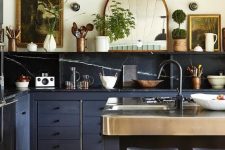a gorgeous eclectic kitchen combining stone backsplash and countertops, navy cabinets and vintage artworks and a mirror