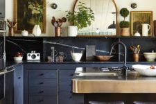 a gorgeous eclectic kitchen combining stone backsplash and countertops, navy cabinets and vintage artworks and a mirror