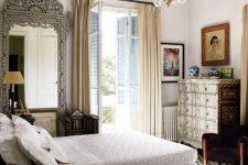 a jaw-dropping guest bedroom with a dark stained bed and an inlay dresser, a fantastic mirror in a carved frame, a modern chandelier and artwork