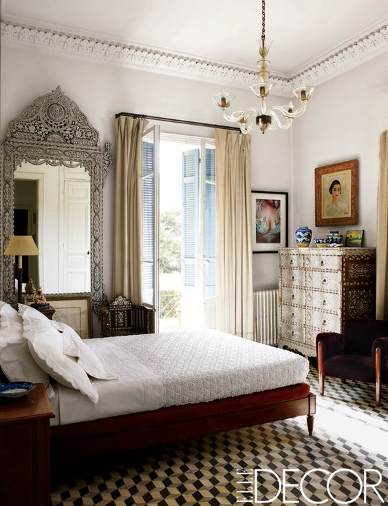 A jaw dropping guest bedroom with a dark stained bed and an inlay dresser, a fantastic mirror in a carved frame, a modern chandelier and artwork