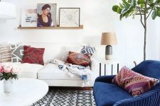 a light-filled eclectic living room with several geometric prints, a navy chair, potted greenery and artworks