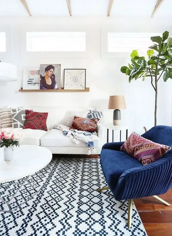 A light-filled eclectic living room with several geometric prints, a navy chair, potted greenery and artworks.