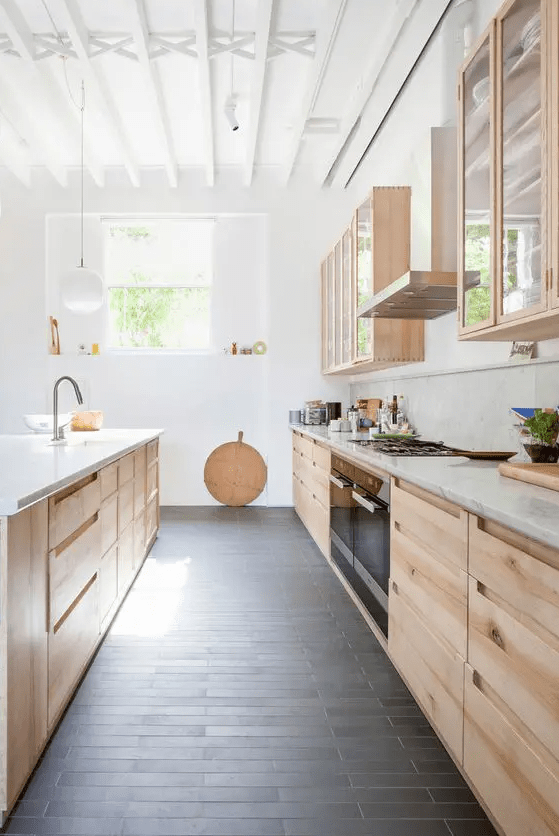 a light-stained galley kitchen with glass cabinets, white stone countertops and a lot of natural light