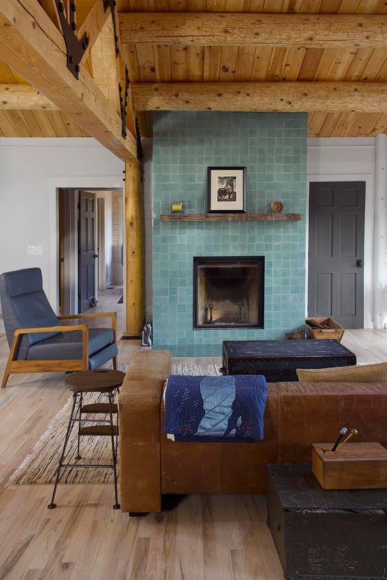 A living room with a stained ceiling, a leather sofa and a fireplace clad with aqua colored Zellige tiles