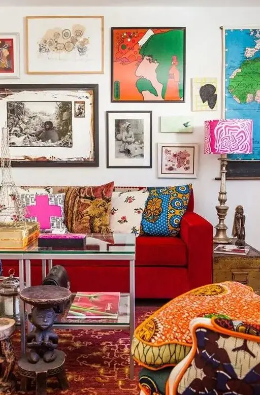 A maximalist living room with a colorful gallery wall, a hot red sofa, a printed chair, a bright rug and some pillows and books.