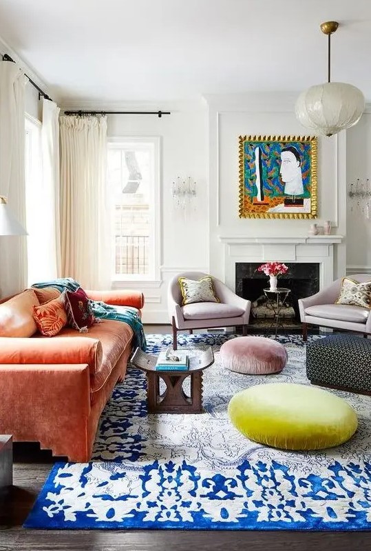 A maximalist living room with a coral sofa, a bold blue rug, pastel ottomans, lilac chairs and a bold artwork.