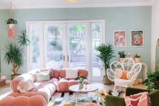 a maximalist living room with a green accent wall, a pink sofa, a green chair, a bright rug and a glazed tiered table