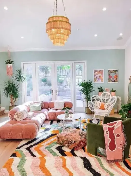 A maximalist living room with a green accent wall, a pink sofa, a green chair, a bright rug and a glazed tiered table.