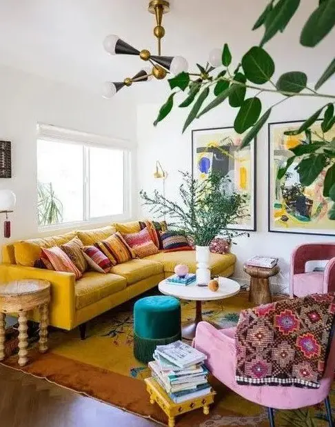 A maximalist living room with a yellow sofa, pink chairs, various tables and bold artworks plus potted plants.