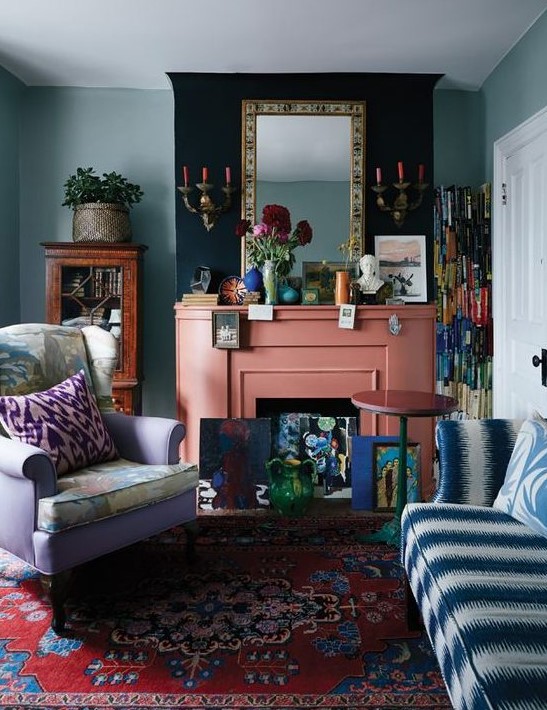 A maximalist living room with green walls, a lilac chair and a blue and white sofa, colorful pillows, a coral fireplace and bright accessories.