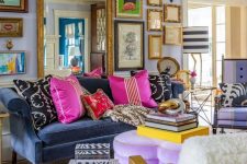 a maximalist living room with lilac walls, a navy sofa, a purple heart ottoman, colorful pillows and books and a gallery wall with a large mirror