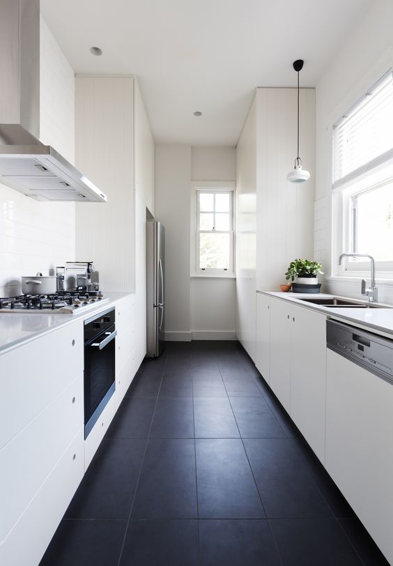 a minimalist white galley kitchen with sleek cabinets,pendant lamps and a black tile floor for a contrast