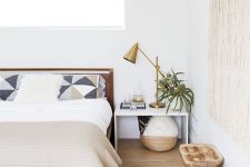 a modern eclectic bedroom with a stained bed and neutral bedding, a brown leather chair, wooden stools, a macrame piece