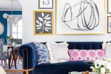 a modern eclectic living room with a navy sofa, amber chairs, a round coffee table, colorful pillows, a free form gallery wall