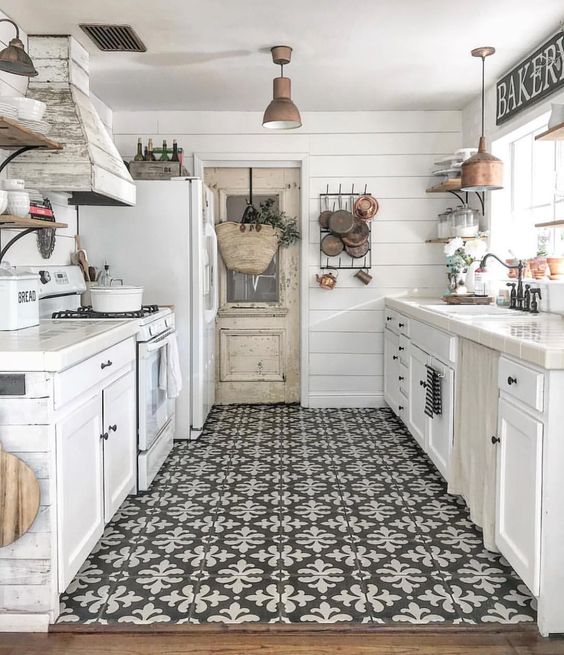 a modern farmhouse galley kitchen with white cabinets, blakc hardware, a mosaic floor and a wooden hood