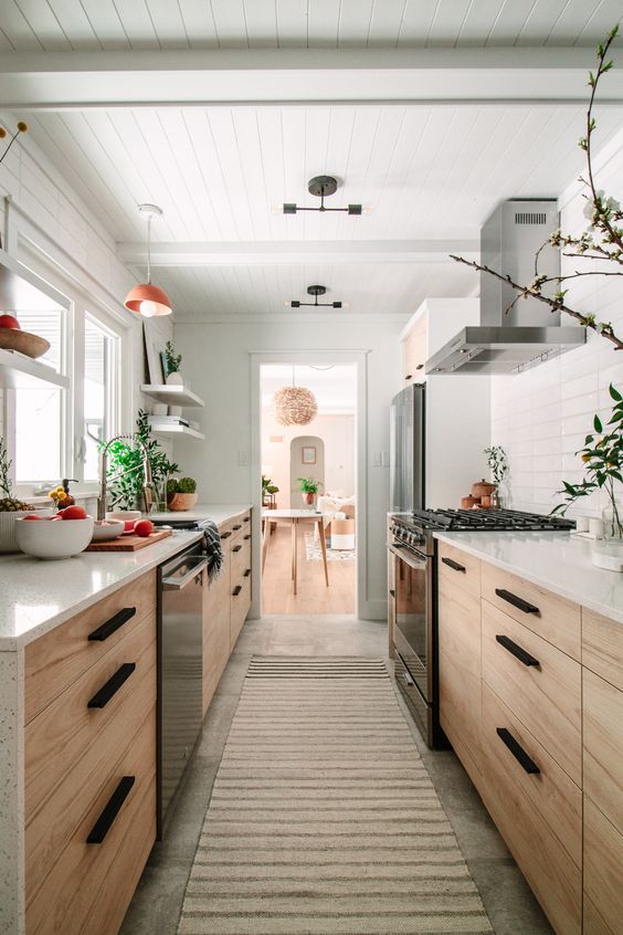 a modern farmhouse stained galley kitchen with white stone countertops and a white tile backsplash, greenery and lots of light