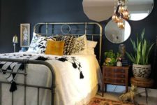 a moody eclectic bedroom with boho rugs and a chandelier, vintage mirrors and a metal bed and mid-century modern nightstands