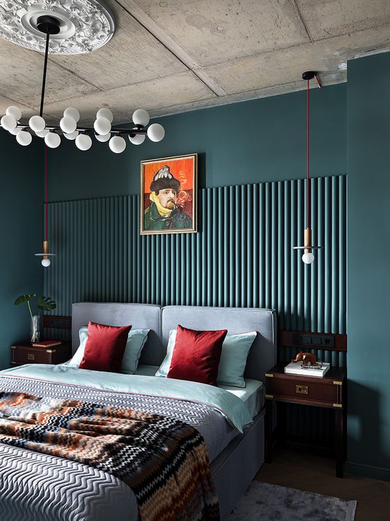 A moody eclectic bedroom with dark green walls and paneling, a dusty blue bed and bold bedding, dark stained nightstands
