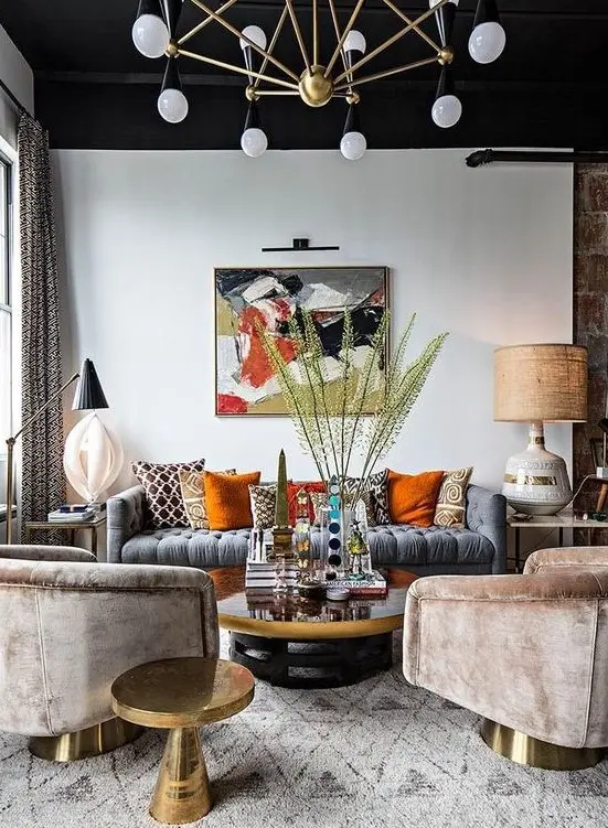 a moody eclectic living area with a black ceiling, colorful pillows, velvet chairs and a brass chandelier
