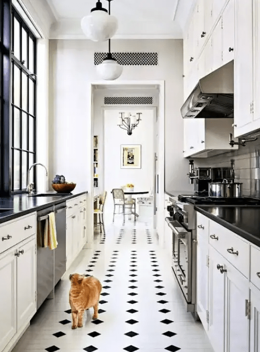 a narrow kitchen with white shaker style cabinets, black countertops, a checked floor and some pendant lamps