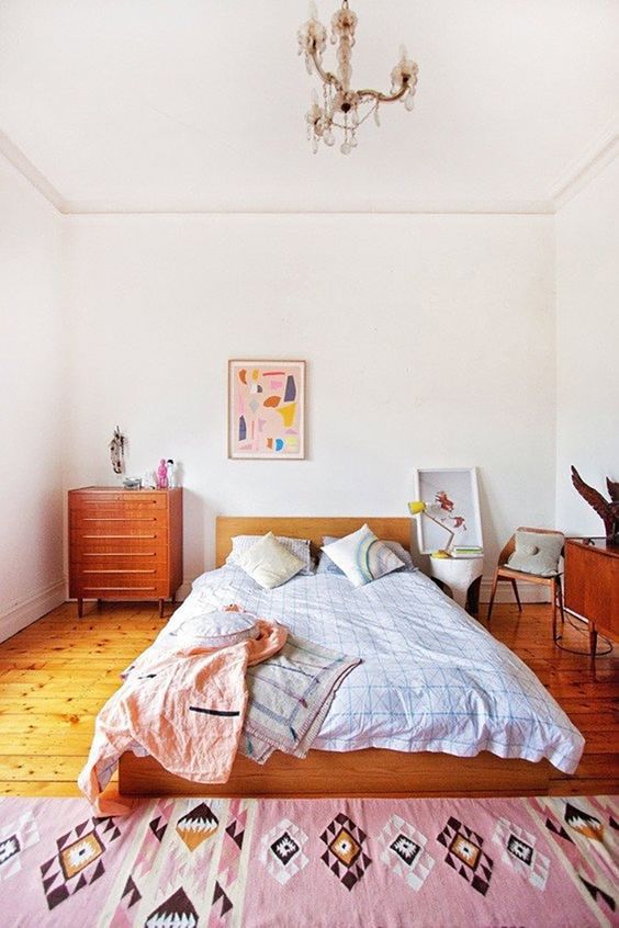 A pretty eclectic bedroom with mid century modern stained furniture, bright textiles and artwork plus a vintage chandelier
