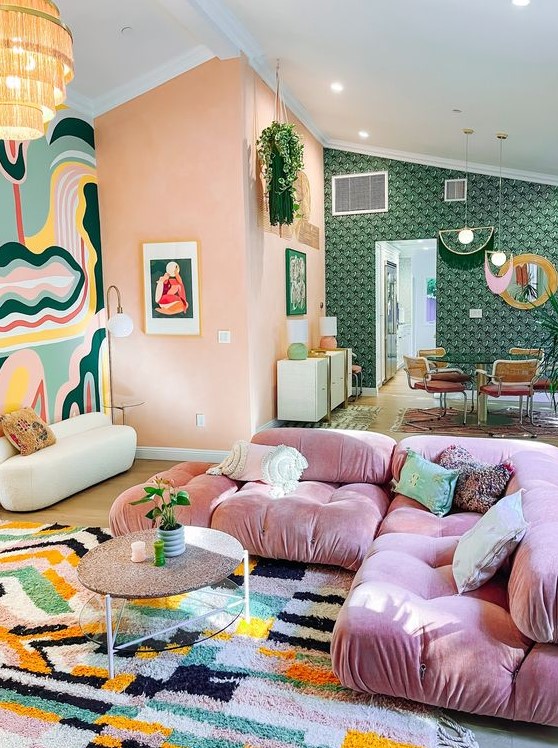 A pretty eclectic living room with coral walls, a bold accent rug, a pink sofa, a coffee table and a bold rug.