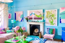 a pretty living room with light blue walls, a pink sofa and a chair, a navy one, a fireplace clad with stone, bold artworks and pillows