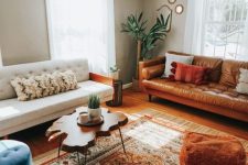 a stylish eclectic living room with grey walls, a white sofa, an amber leather sofa, a bold printed rug, a living edge coffee table