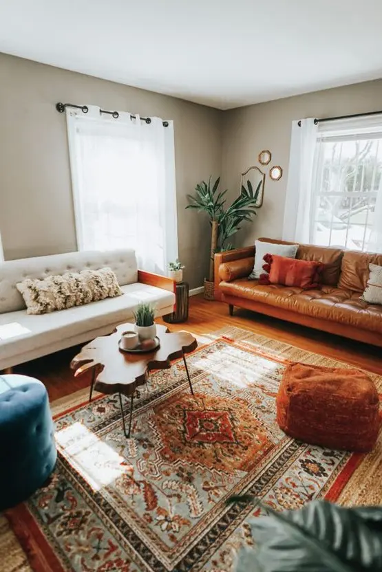 A stylish eclectic living room with grey walls, a white sofa, an amber leather sofa, a bold printed rug, a living edge coffee table.